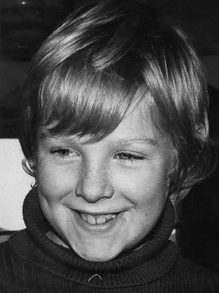 Black and white photo of Alex aged eight, smiling, in a polo-neck jumper