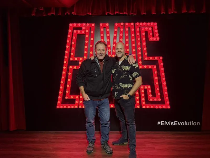 Alex, left, and his brother Jack, arms round each other, in front of a giant red light-bulb ELVIS sign