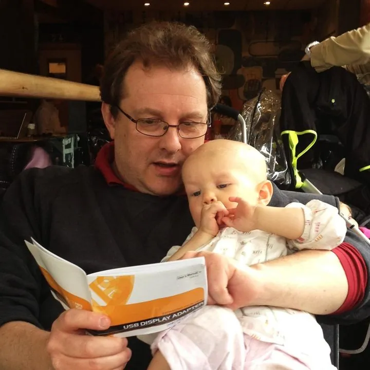Alex holding baby Lizzy on his lap as they look at a booklet together in a café