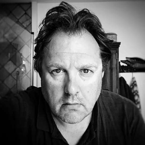 Black and white portrait of Alex Bremer, dark hair swept back, looking straight into the camera
