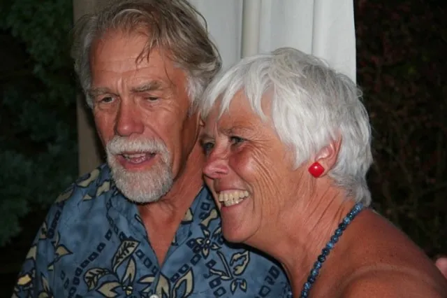 Nick Bremer, white-bearded in a blue patterned shirt, cheek to cheek with a laughing Jill, who has short white hair and red earrings