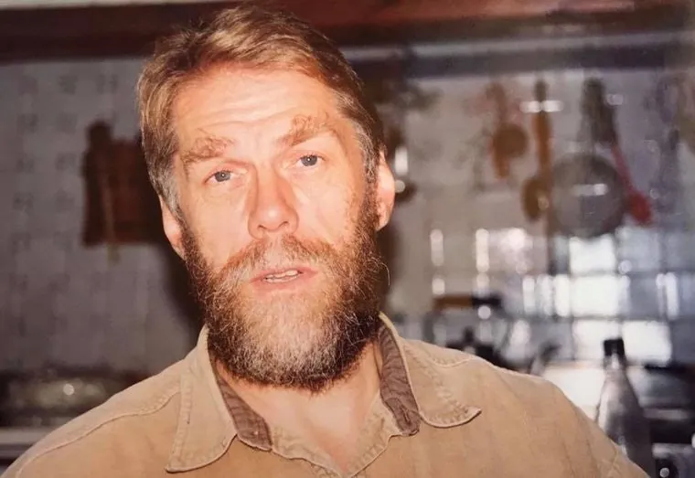 Colour photo of Nick Bremer with a full reddish beard, in a tan shirt, in a kitchen