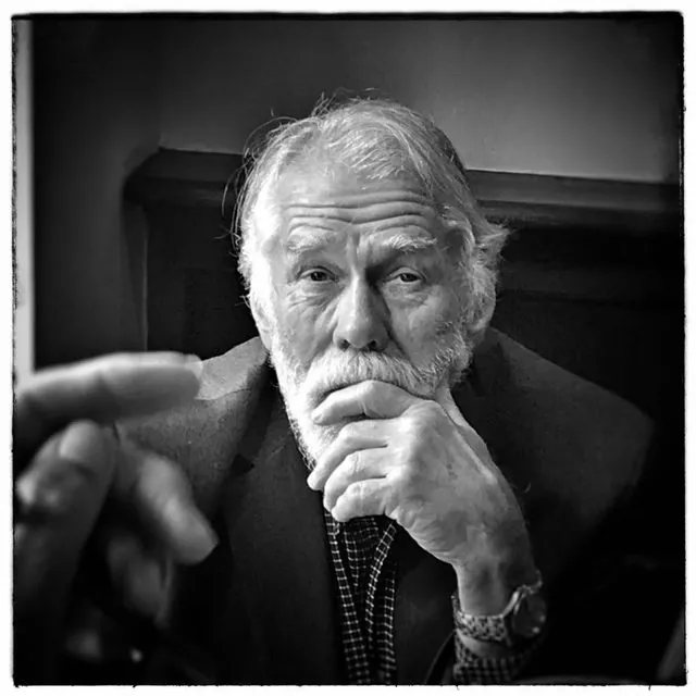 Black and white portrait of Nick Bremer, white-haired and bearded, chin resting on his hand